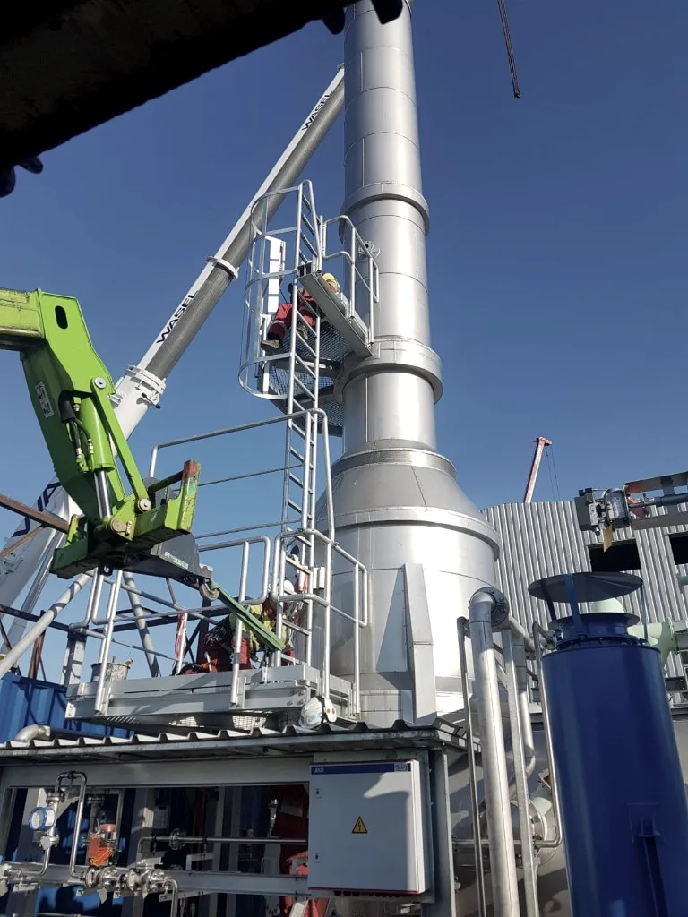 Monteur auf der Arbeitsbühne am Schornstein, Hubarbeitsbühne daneben